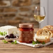 Artisanal Greek appetizer pairing of Navarino Icons stuffed peppers with cream cheese, a block of feta, olives, fresh bread, and a glass of white wine.