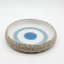 Handmade ceramic bowl with a speckled exterior and a blue "evil eye" concentric circle design on a white background.